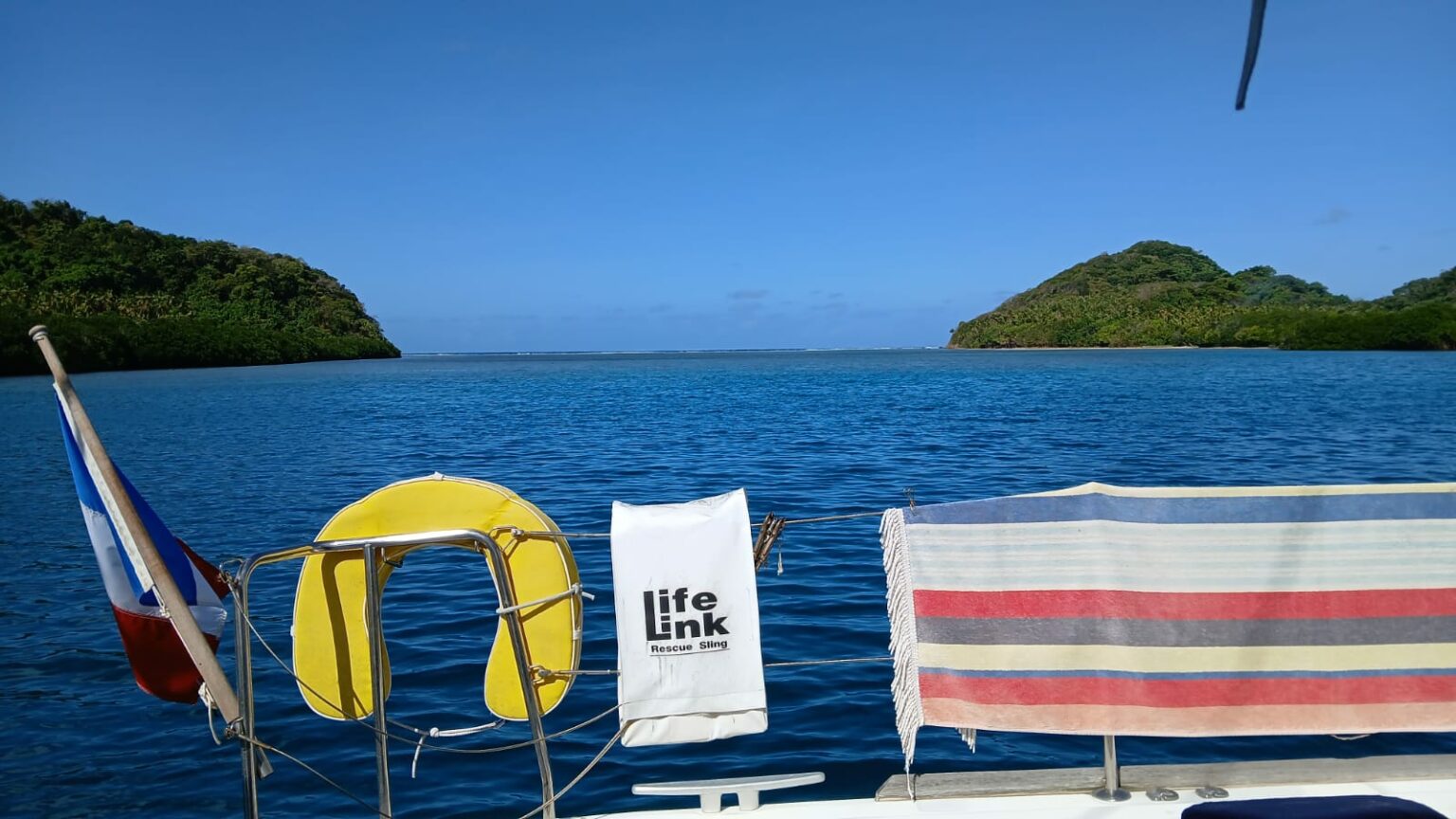 A yellow lifebuoy and a French flag on the stern rail, islands behind