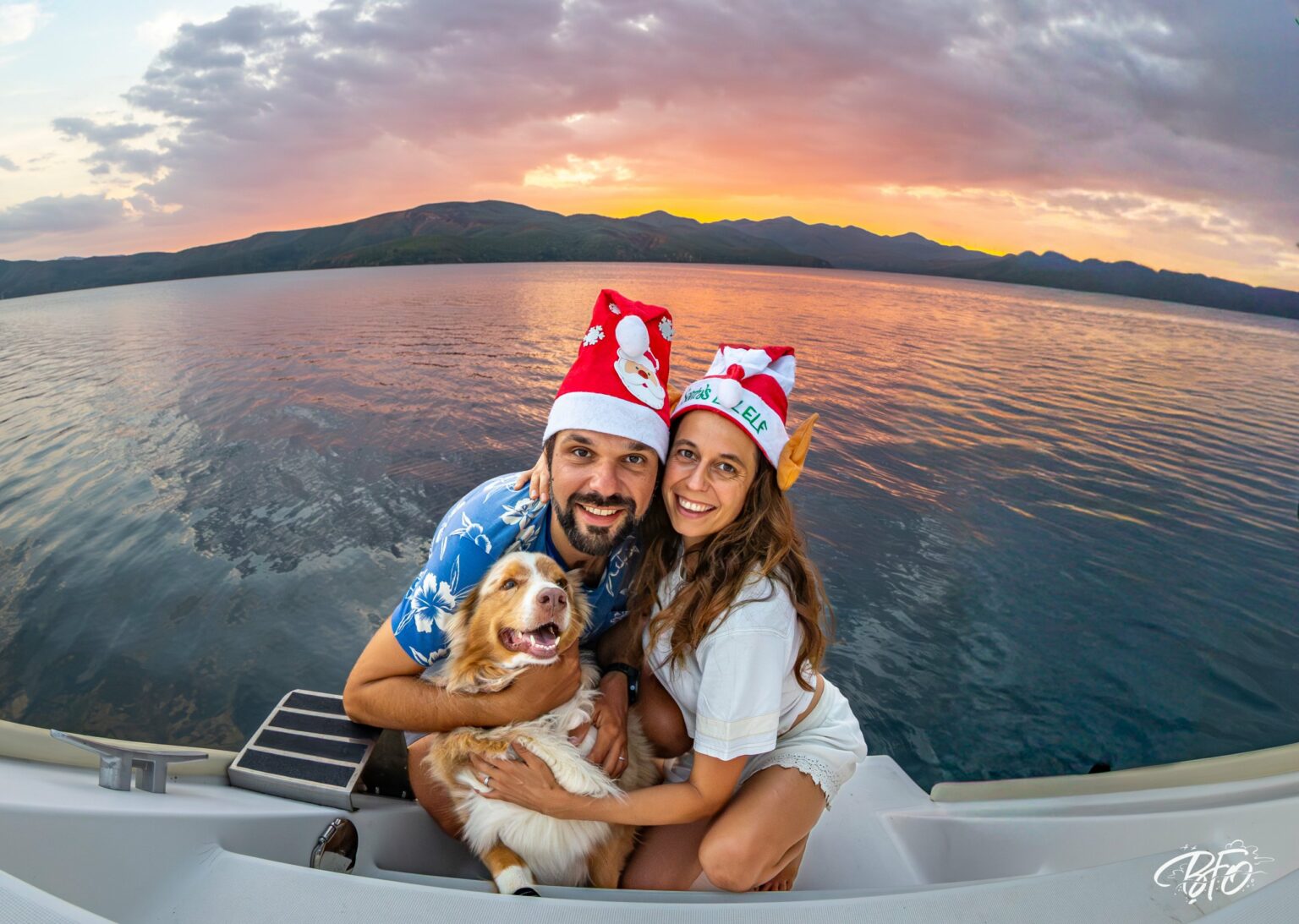 Two crew members and the dog in Christmas hats on the stern at sunset