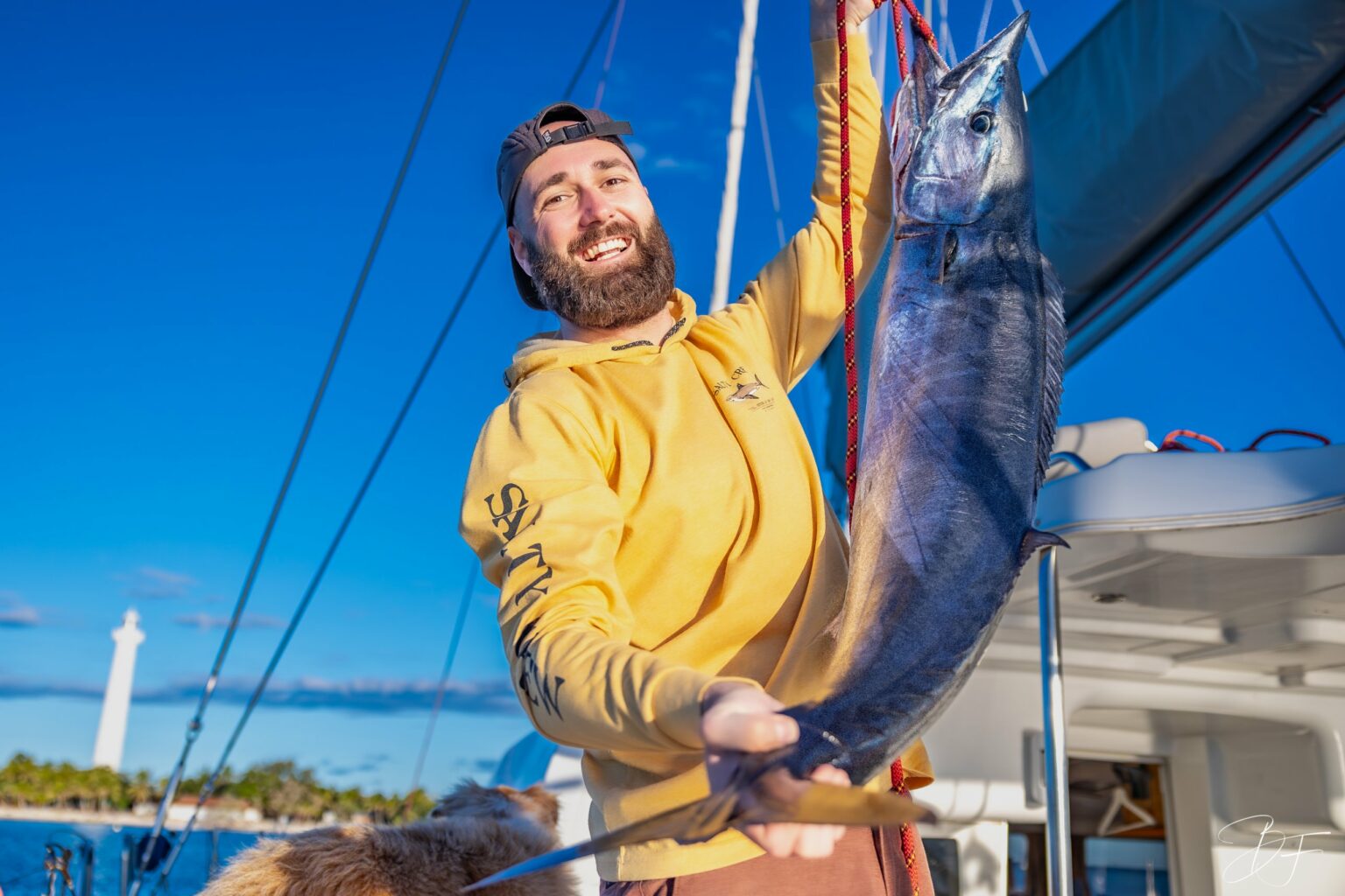 A crew member holds up a fish caught aboard myCloud, lighthouse in the background