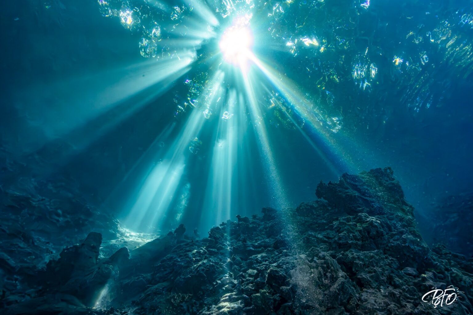 Beams of light cutting through turquoise water above rocks and corals