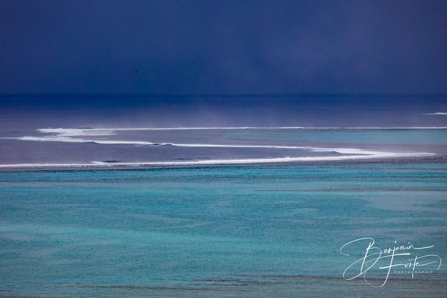 Line of surf on the barrier reef, turquoise lagoon and dark squall